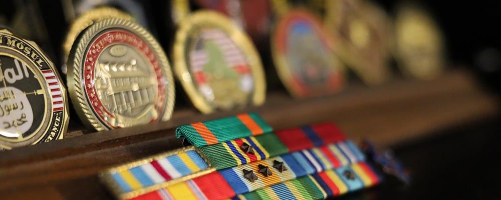 Challenge coins displayed on a wood base with military ribbons.